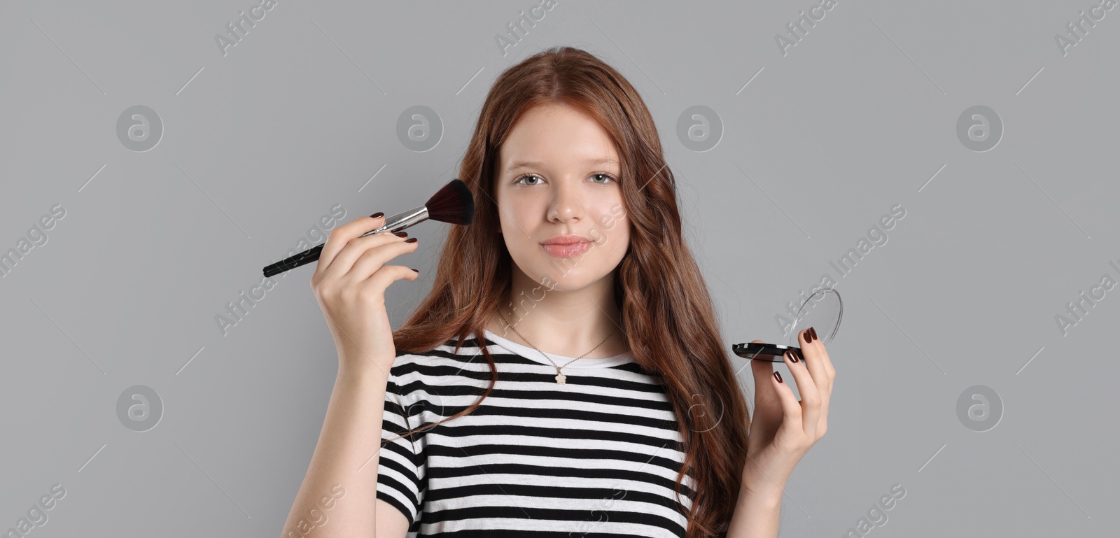 Photo of Teenage girl applying blusher with makeup brush on grey background