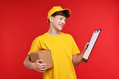 Photo of Teenage boy with parcel and clipboard working as courier on red background