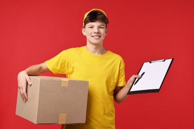 Photo of Teenage boy with parcel and clipboard working as courier on red background