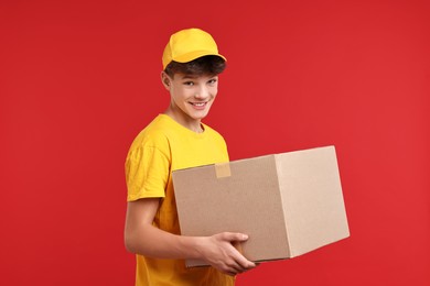 Photo of Teenage boy with parcel working as courier on red background