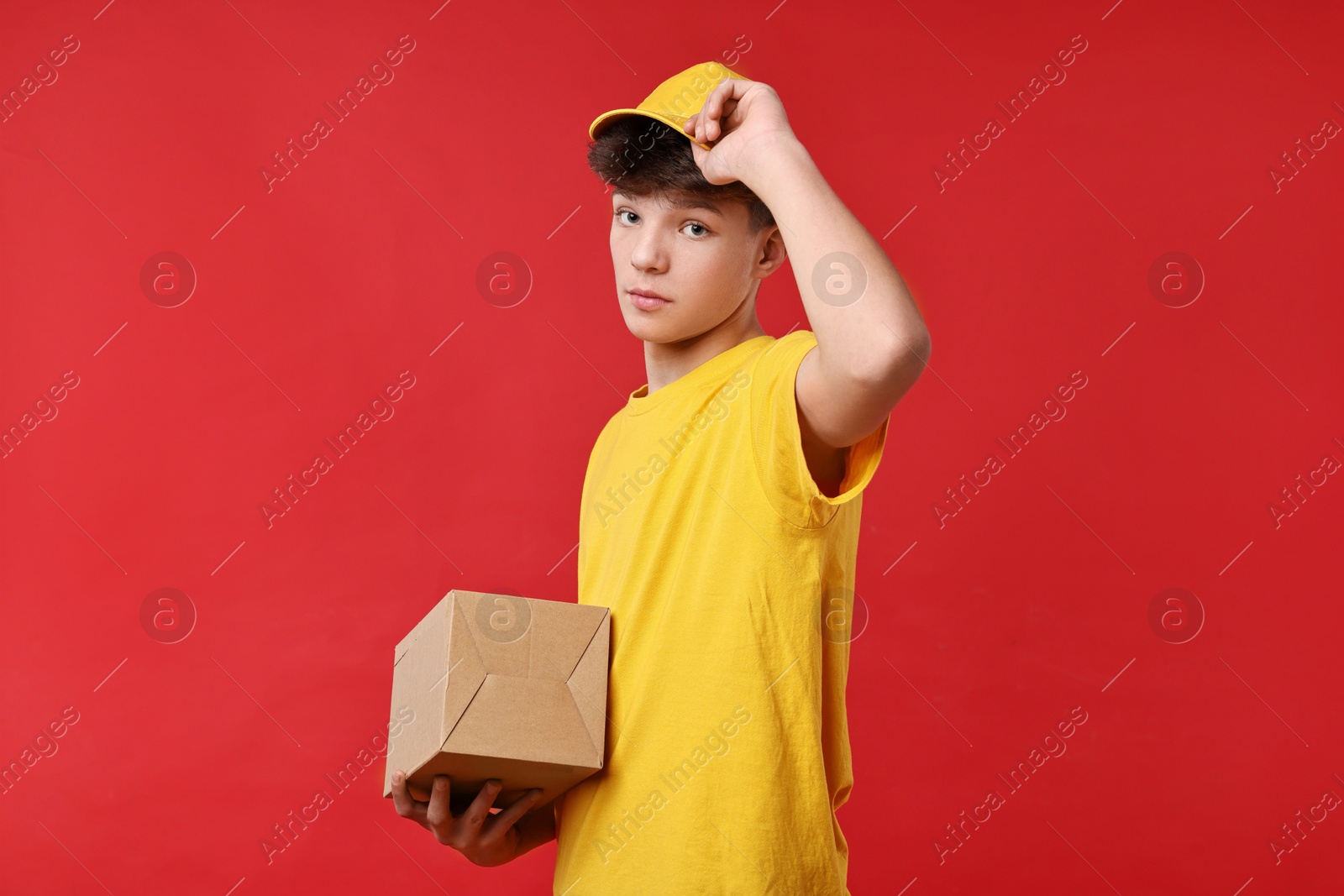 Photo of Teenage boy with parcel working as courier on red background