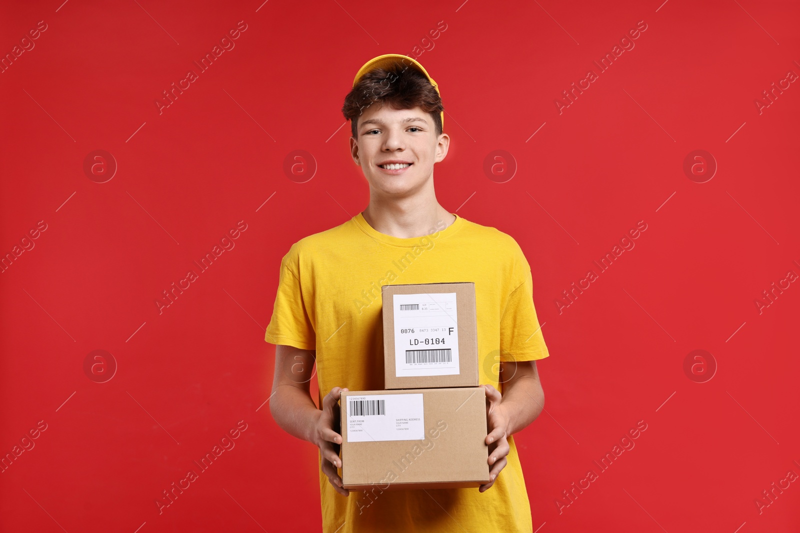 Photo of Teenage boy with parcels working as courier on red background