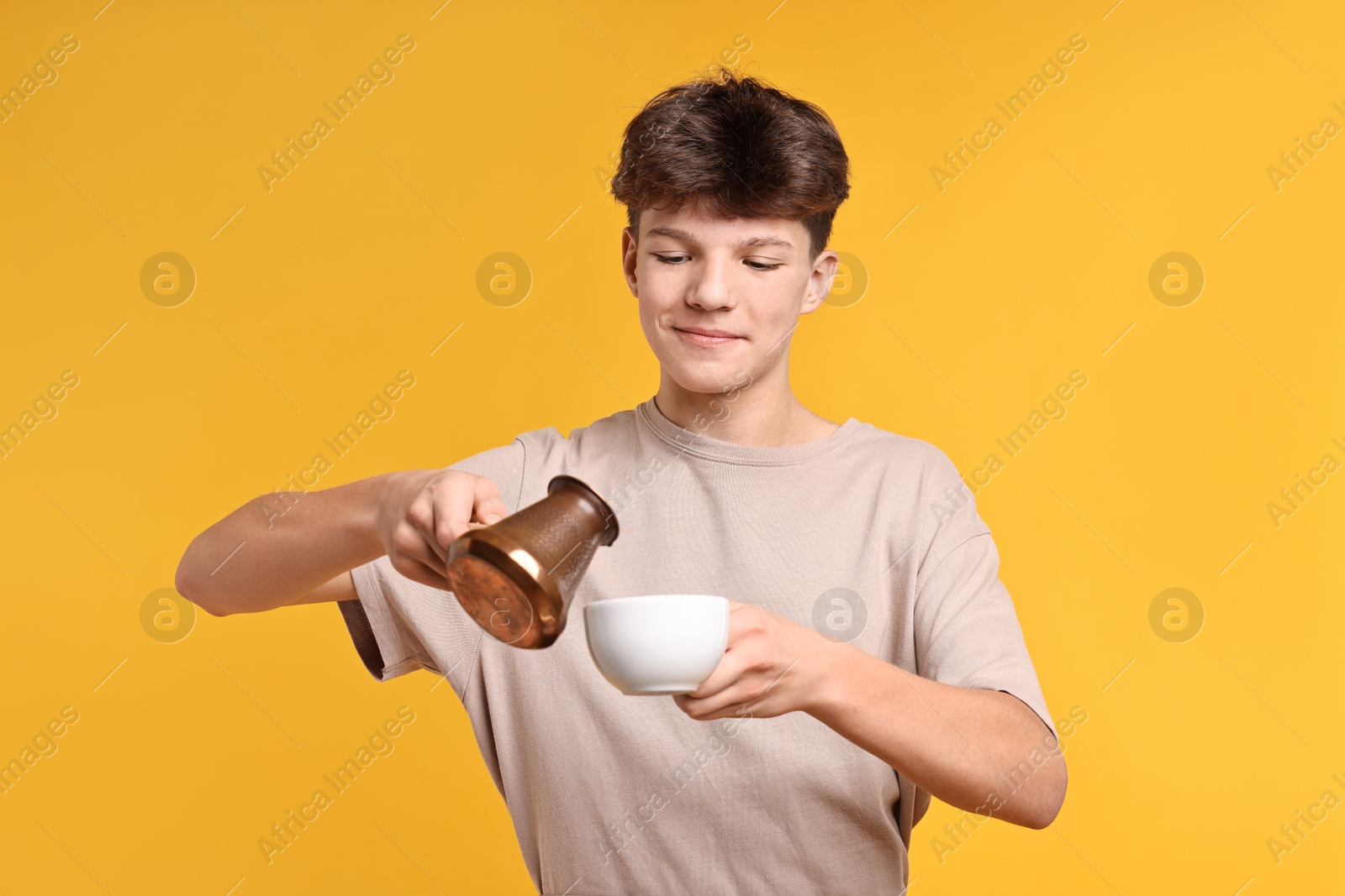 Photo of Teenage boy with cezve pot and cup working as barista on orange background