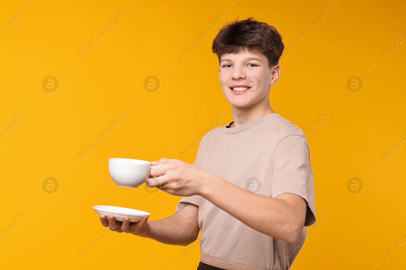 Photo of Teenage boy with cup working as barista on orange background