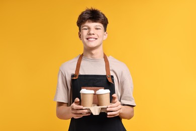 Photo of Teenage boy with paper cups working as barista on orange background