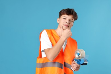 Photo of Teenage boy with tape gun dispenser in safety vest working as warehouse packer on blue background