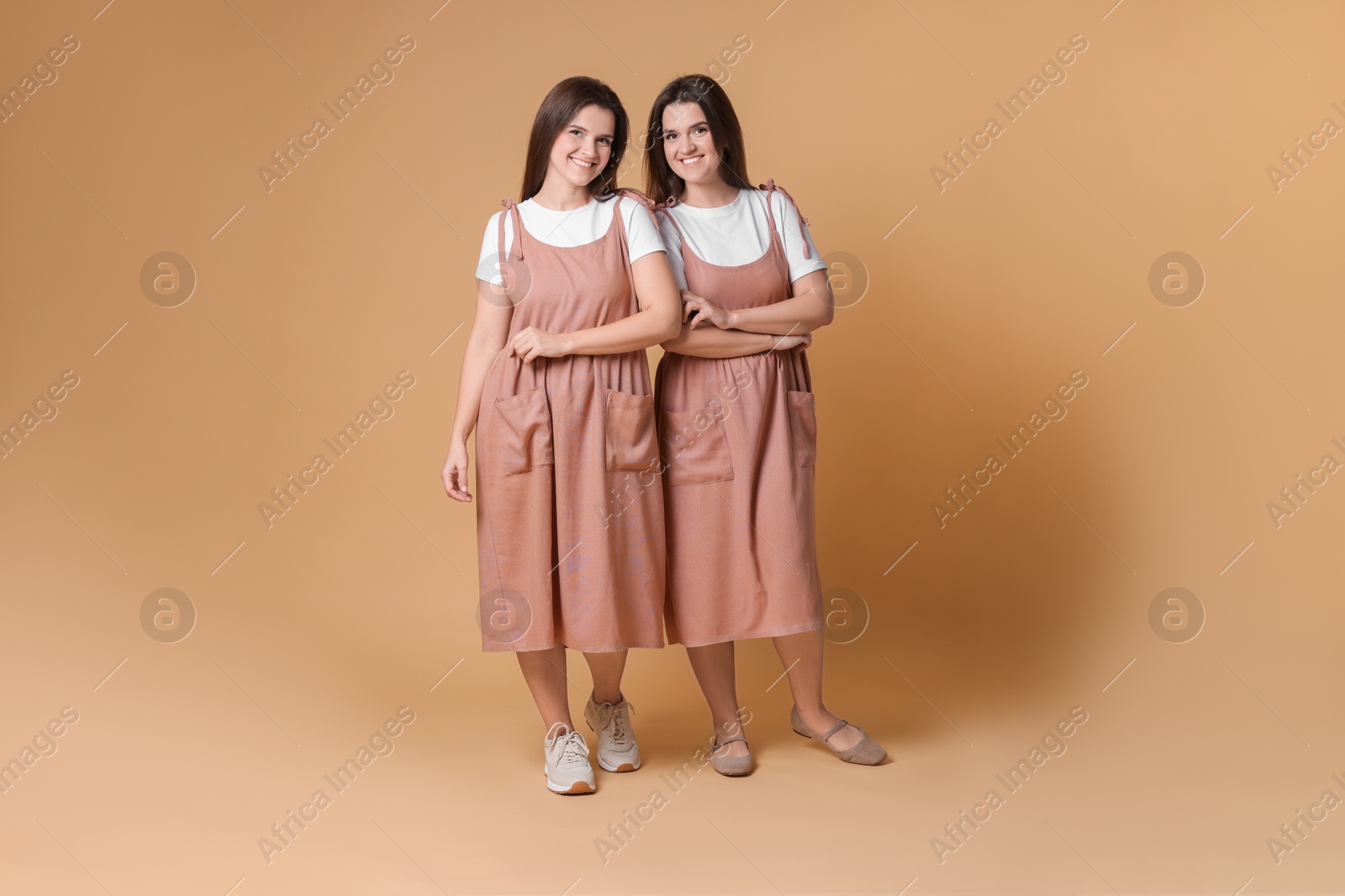 Photo of Portrait of happy twin sisters on pale brown background