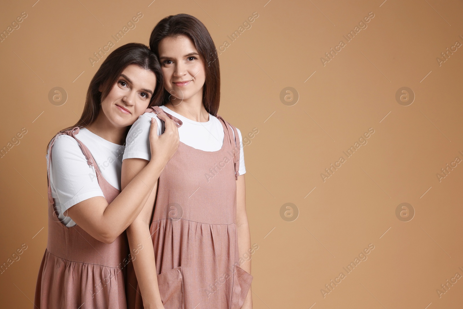 Photo of Portrait of beautiful twin sisters on pale brown background, space for text