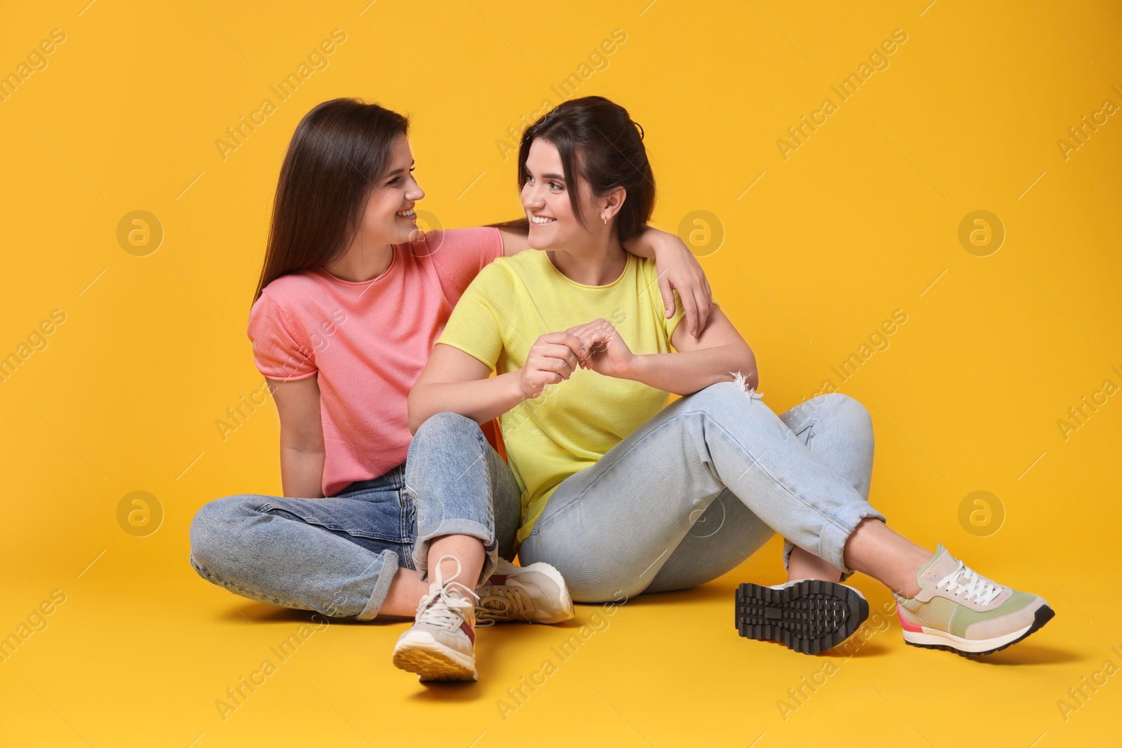 Photo of Portrait of happy twin sisters on orange background