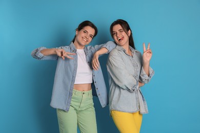 Photo of Portrait of beautiful twin sisters showing peace signs on light blue background