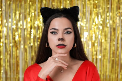 Photo of Beautiful woman with cat makeup and ears on golden background