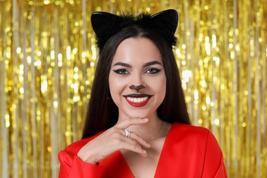 Photo of Beautiful woman with cat makeup and ears on golden background