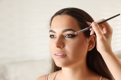 Photo of Artist doing beautiful makeup on woman's face indoors