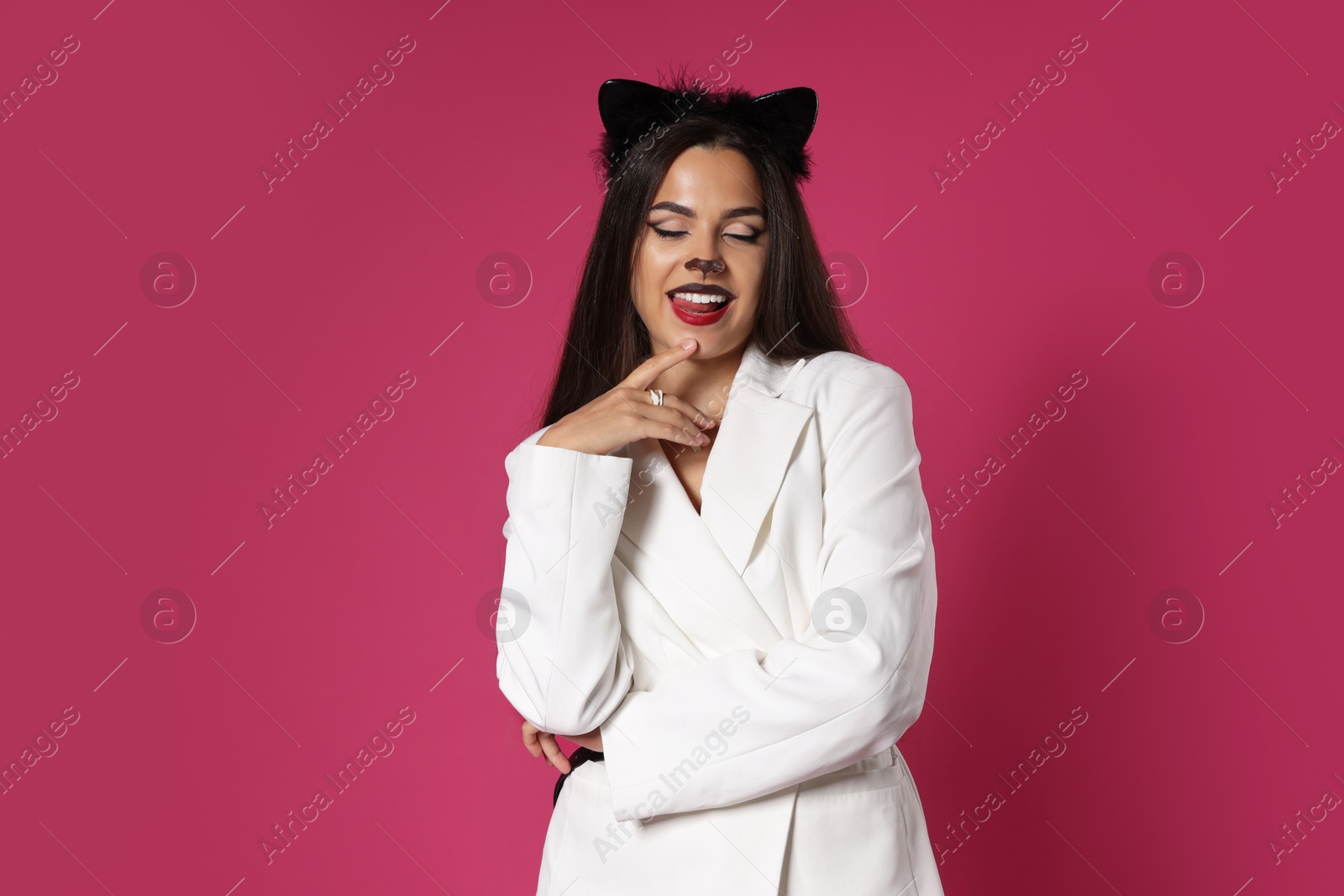 Photo of Charming woman with cat makeup and ears in stylish outfit on pink background