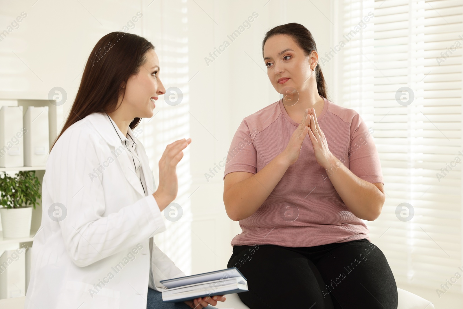 Photo of Nutritionist with notebook giving recommendations to overweight woman in hospital