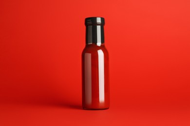 Photo of Ketchup in glass bottle on red background