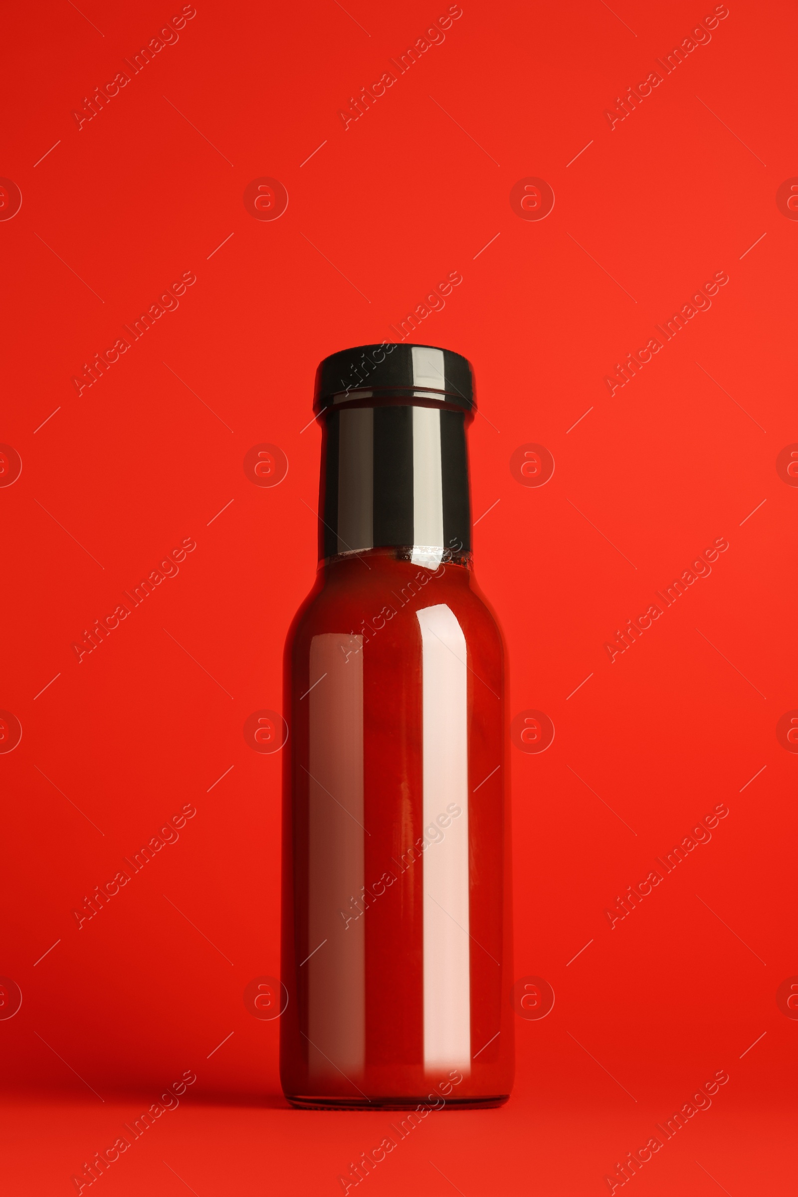 Photo of Ketchup in glass bottle on red background