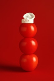 Photo of Stack of fresh tomatoes with plastic cap as bottle of ketchup on red background