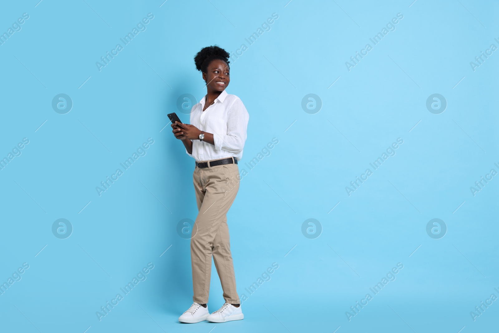 Photo of Happy woman with smartphone on light blue background. Space for text