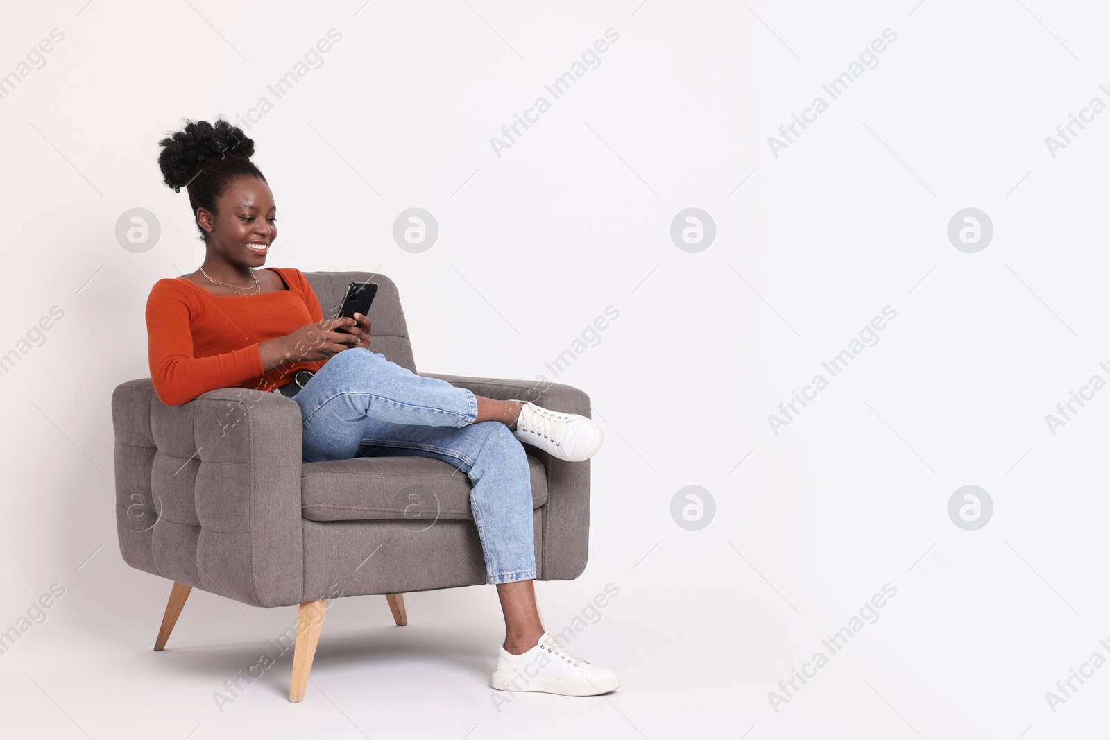 Photo of Smiling woman with smartphone sitting in armchair on white background. Space for text