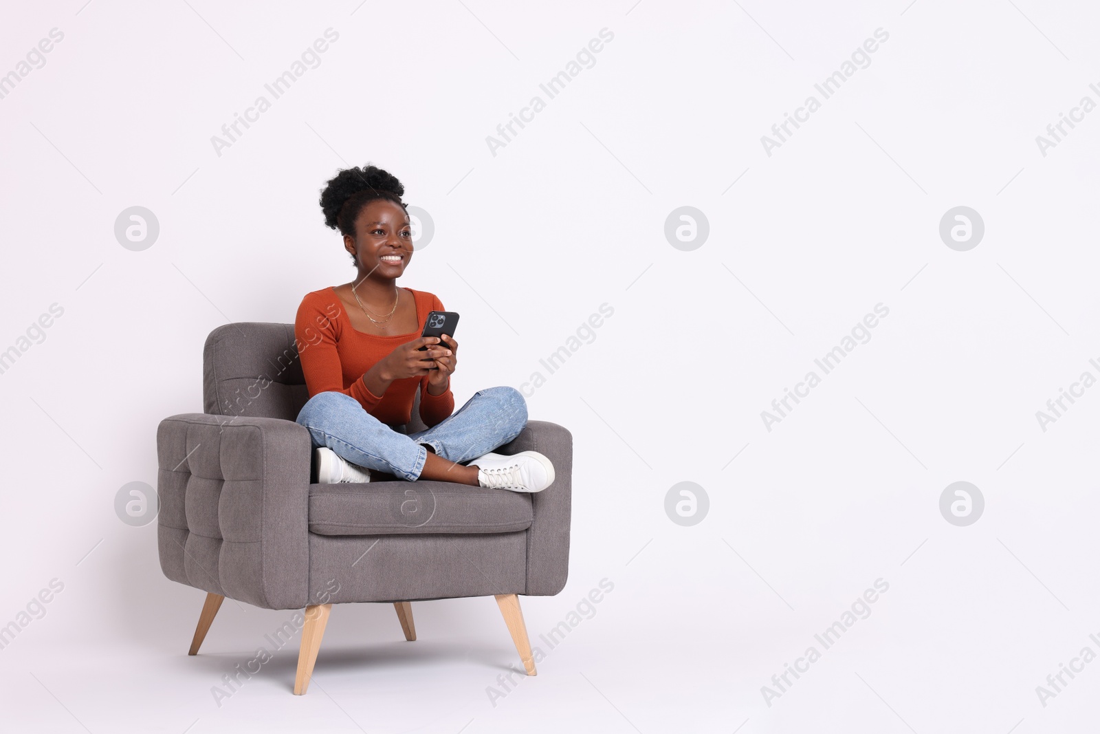 Photo of Smiling woman with smartphone sitting in armchair on white background. Space for text