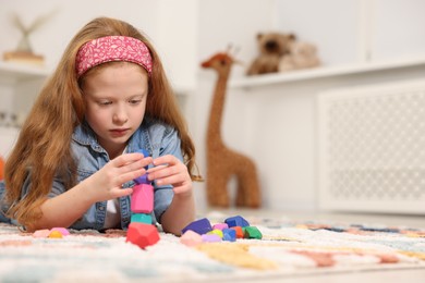 Photo of Little girl building tower with balancing stones on floor indoors, space for text