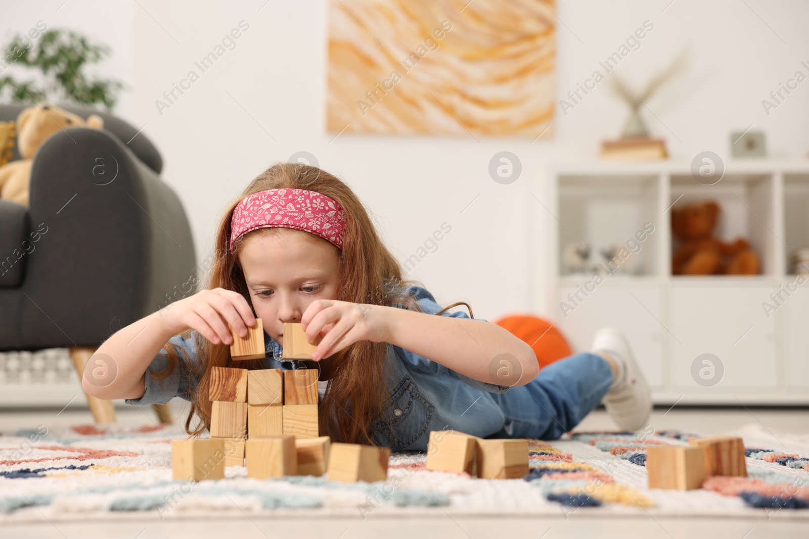 Photo of Little girl playing with wooden cubes on floor indoors