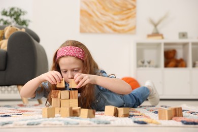 Photo of Little girl playing with wooden cubes on floor indoors