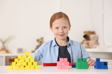 Photo of Little girl playing with colorful cubes at white table indoors