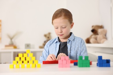 Photo of Little girl playing with colorful cubes at white table indoors