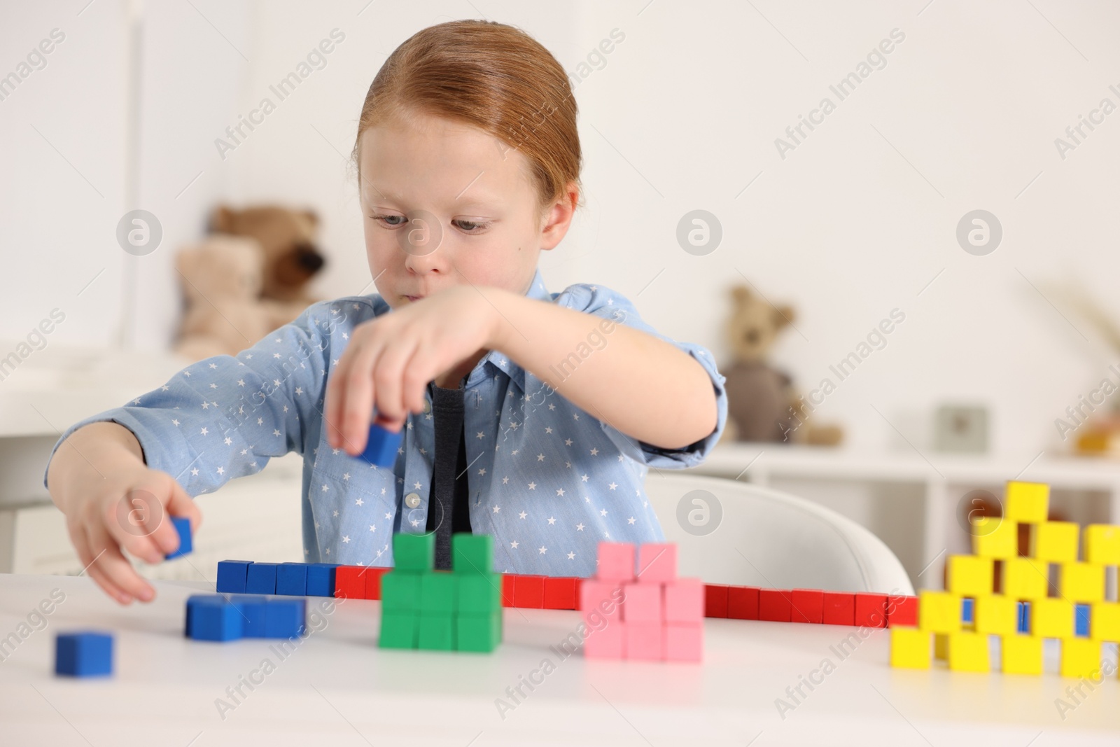 Photo of Little girl playing with colorful cubes at white table indoors