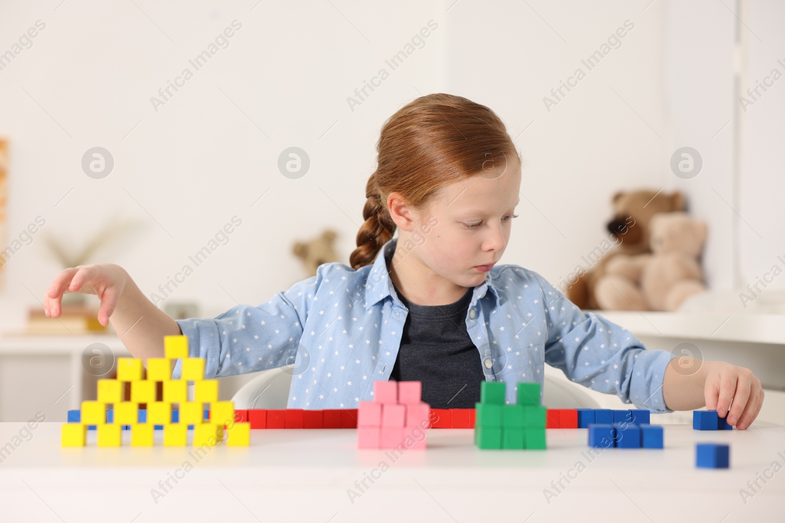 Photo of Little girl playing with colorful cubes at white table indoors