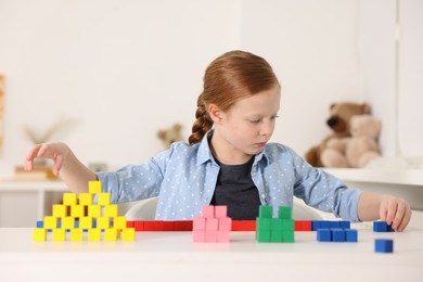 Photo of Little girl playing with colorful cubes at white table indoors