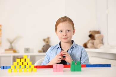 Photo of Little girl playing with colorful cubes at white table indoors