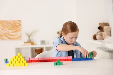 Photo of Little girl playing with colorful cubes at white table indoors