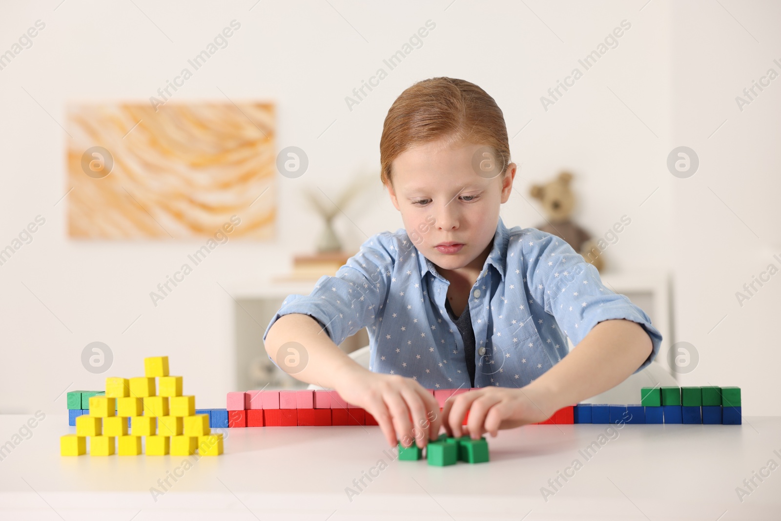 Photo of Little girl playing with colorful cubes at white table indoors