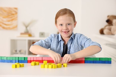 Photo of Little girl playing with colorful cubes at white table indoors