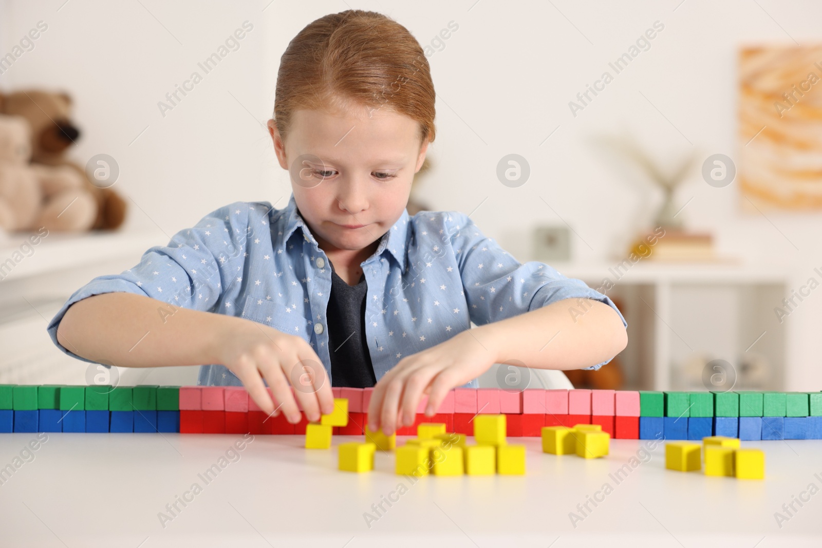 Photo of Little girl playing with colorful cubes at white table indoors