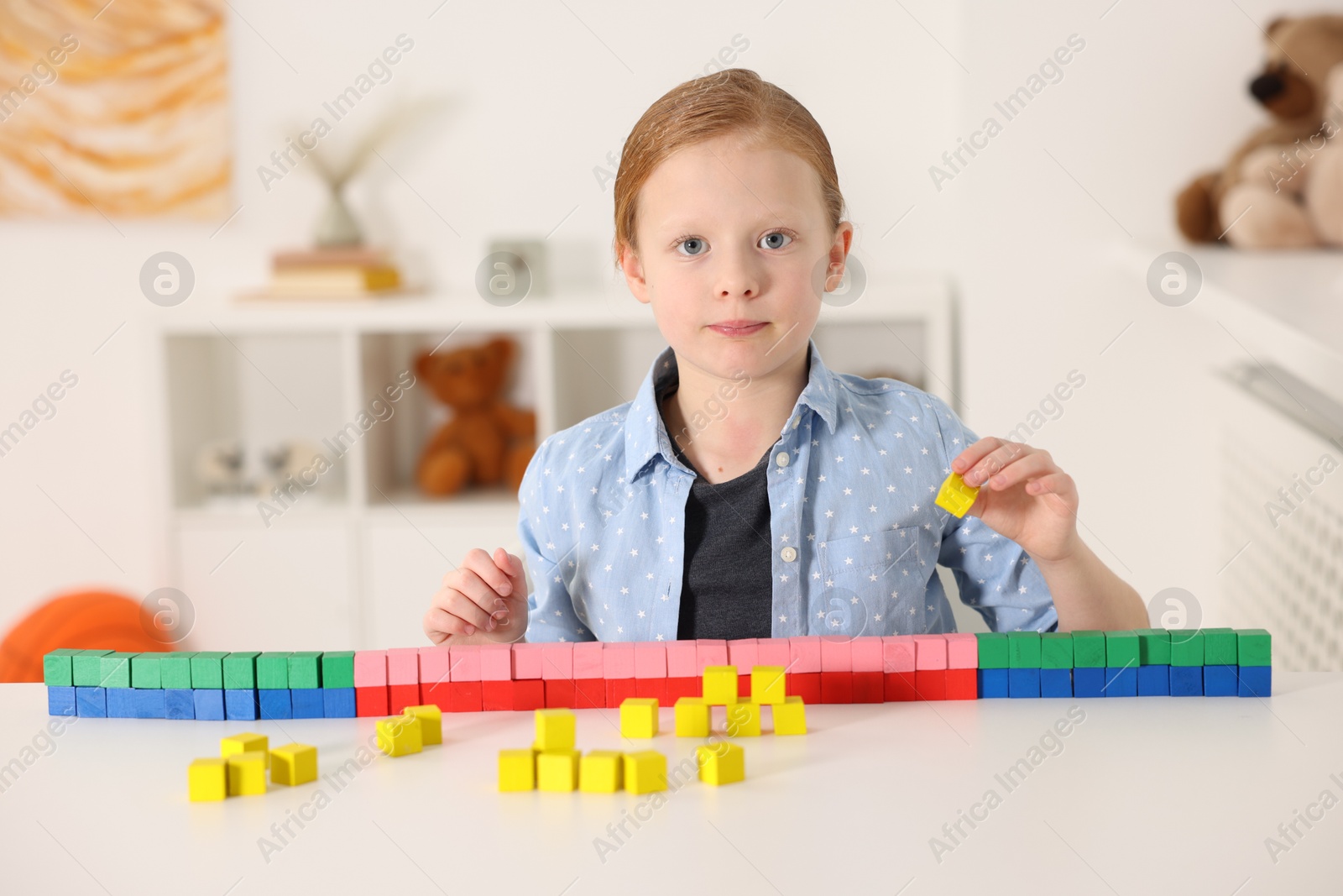 Photo of Little girl playing with colorful cubes at white table indoors