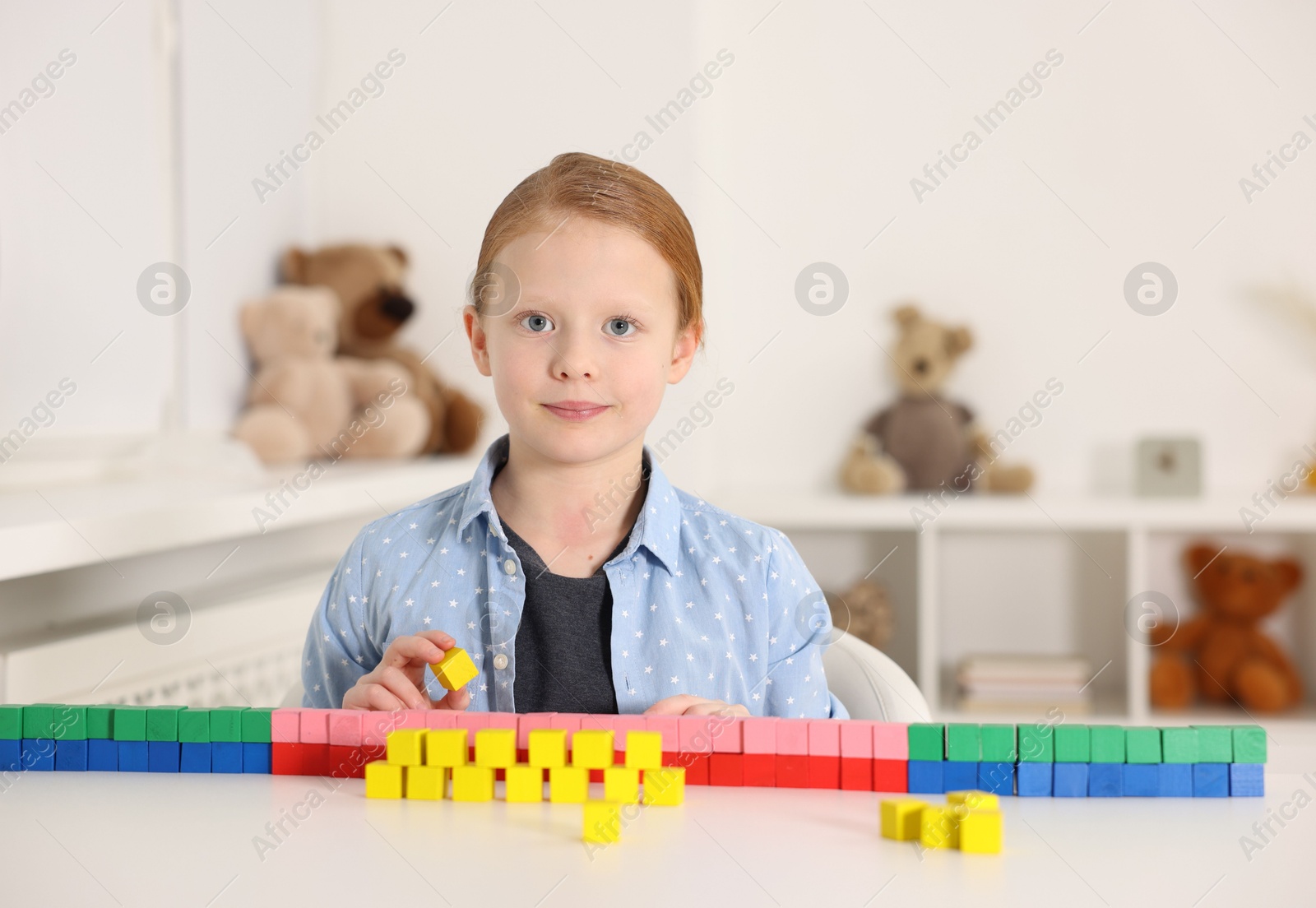 Photo of Little girl playing with colorful cubes at white table indoors