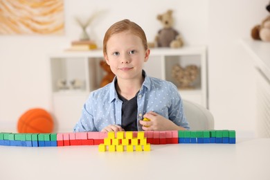 Photo of Little girl playing with colorful cubes at white table indoors