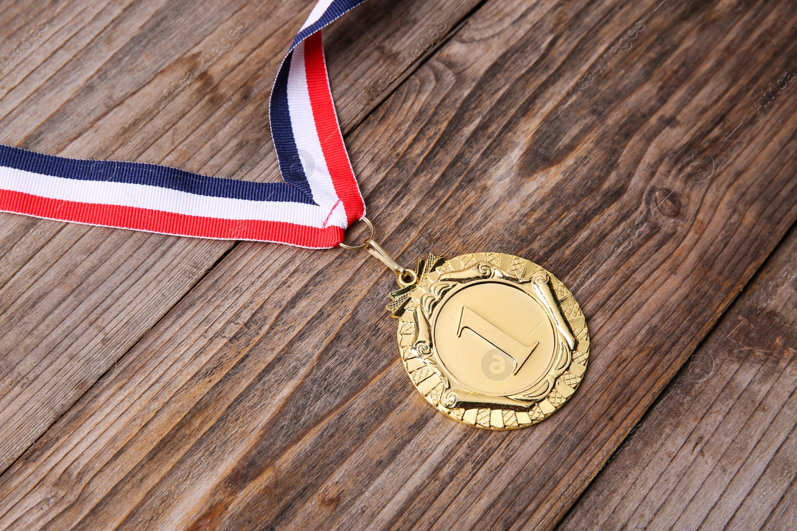 Photo of Golden medal with striped ribbon on wooden background, closeup