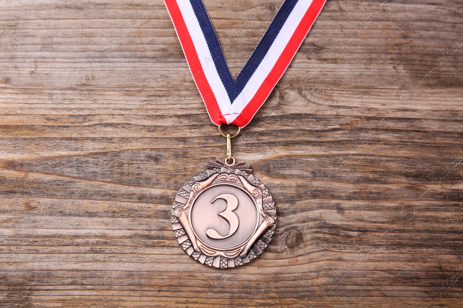 Photo of Bronze medal with striped ribbon on wooden background, top view