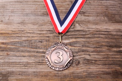 Photo of Bronze medal with striped ribbon on wooden background, top view