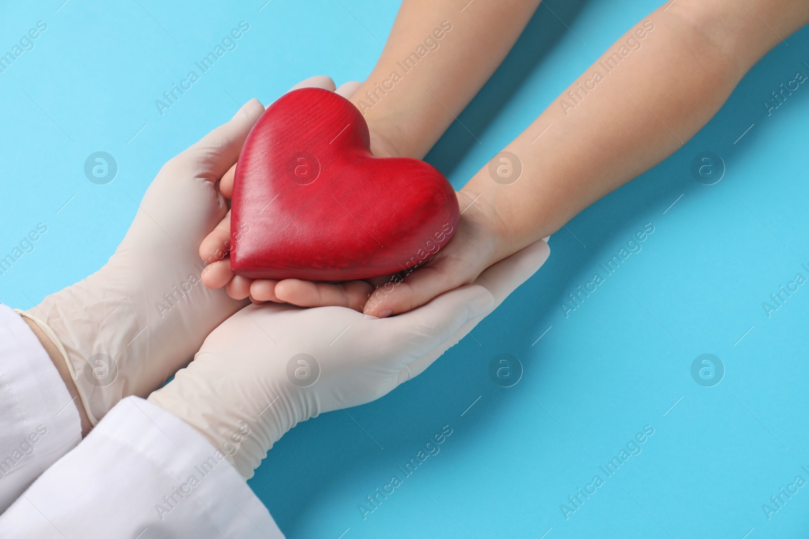 Photo of Doctor and child holding heart model on light blue background, closeup