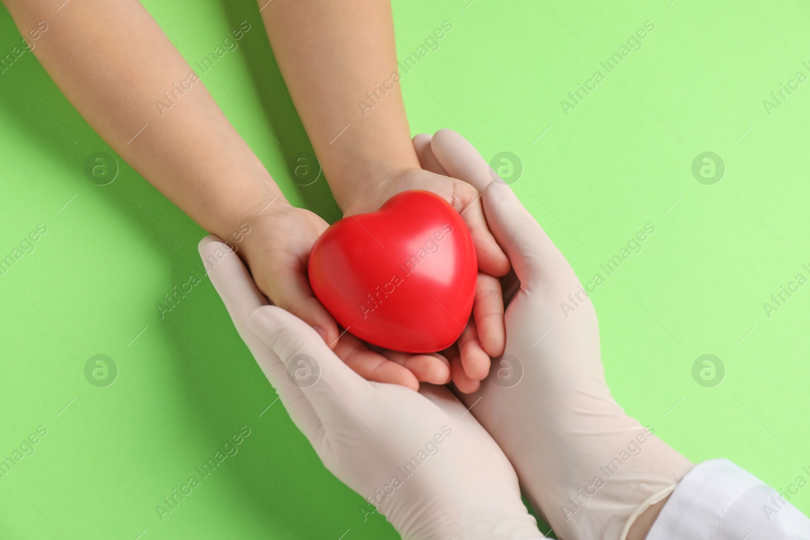 Photo of Doctor and child holding heart model on light green background, top view