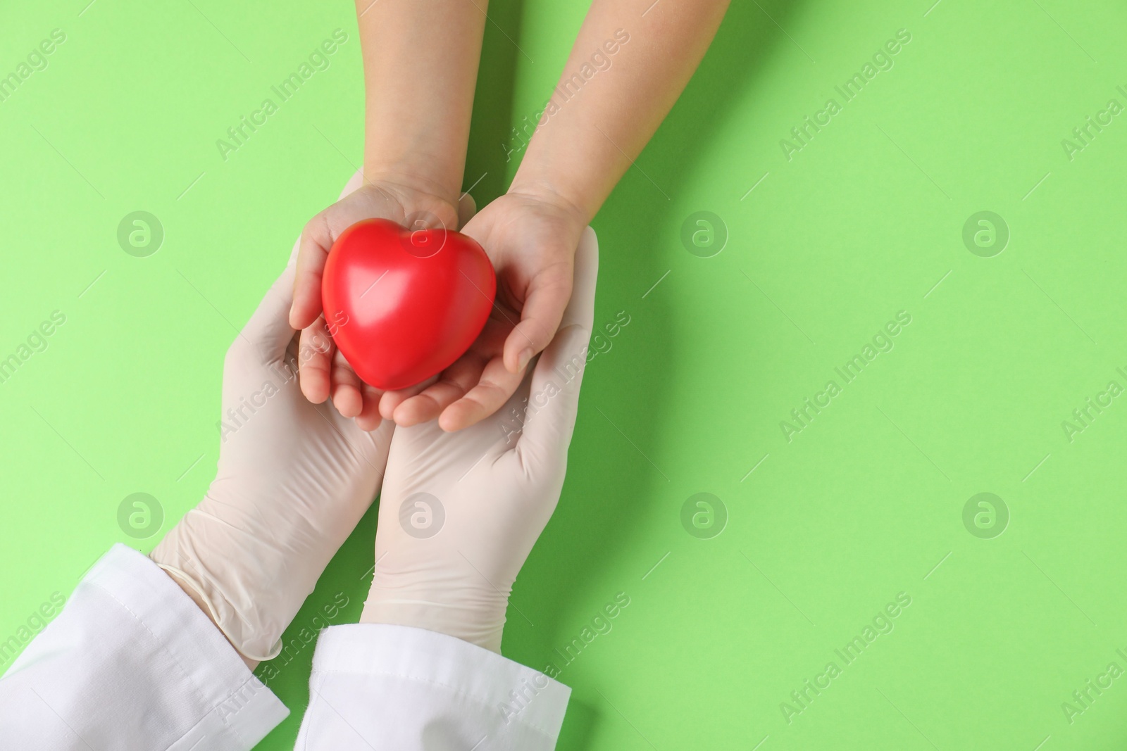 Photo of Doctor and child holding heart model on light green background, top view. Space for text