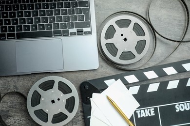 Photo of Flat lay composition with movie clapper, film reels and laptop on grey textured table