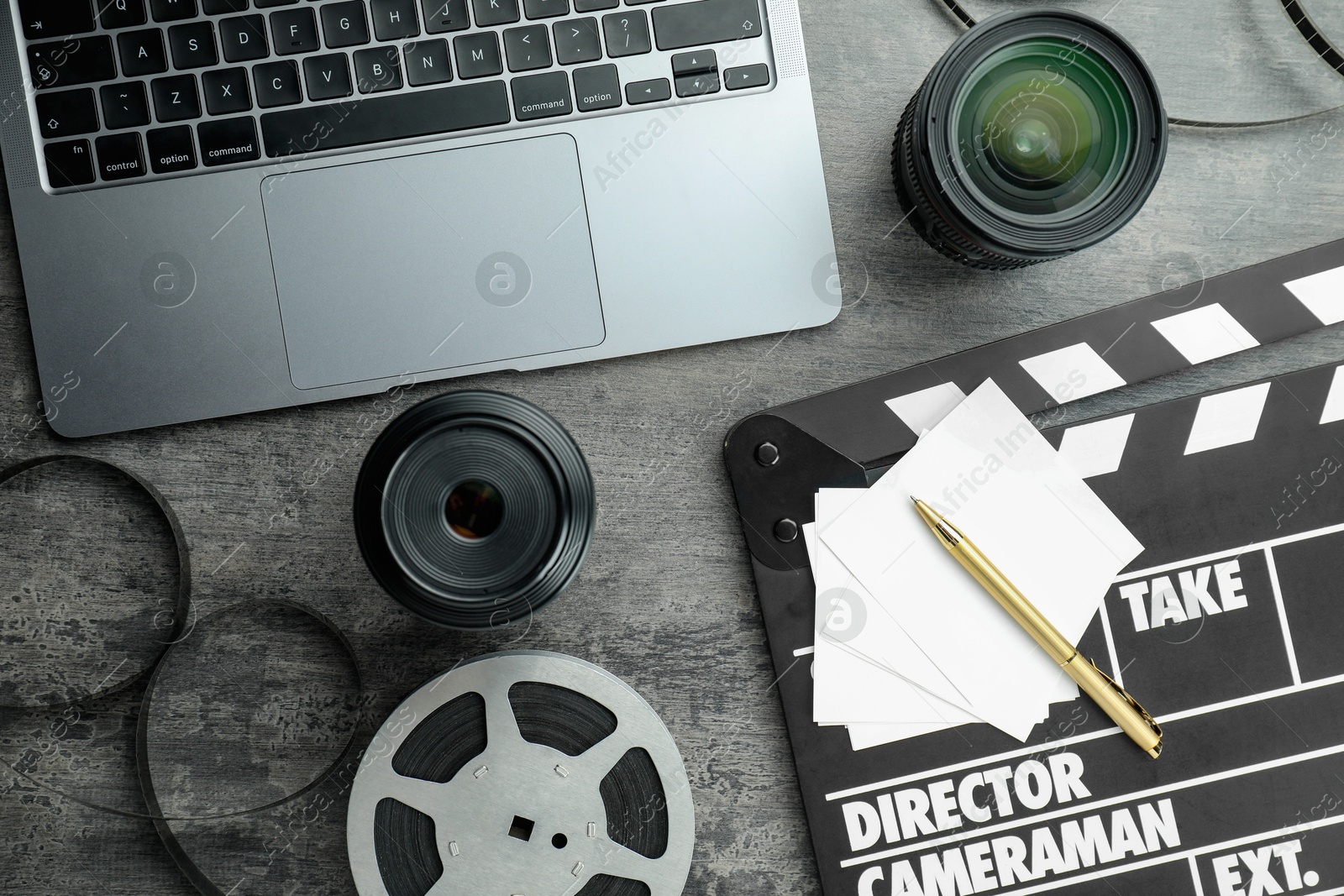 Photo of Flat lay composition with movie clapper, film reel and camera lens on grey textured table