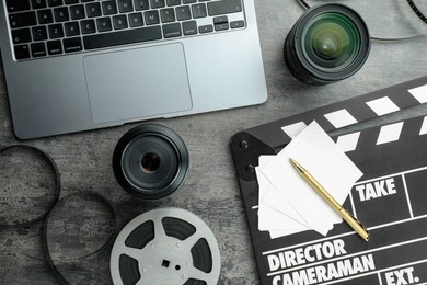 Photo of Flat lay composition with movie clapper, film reel and camera lens on grey textured table